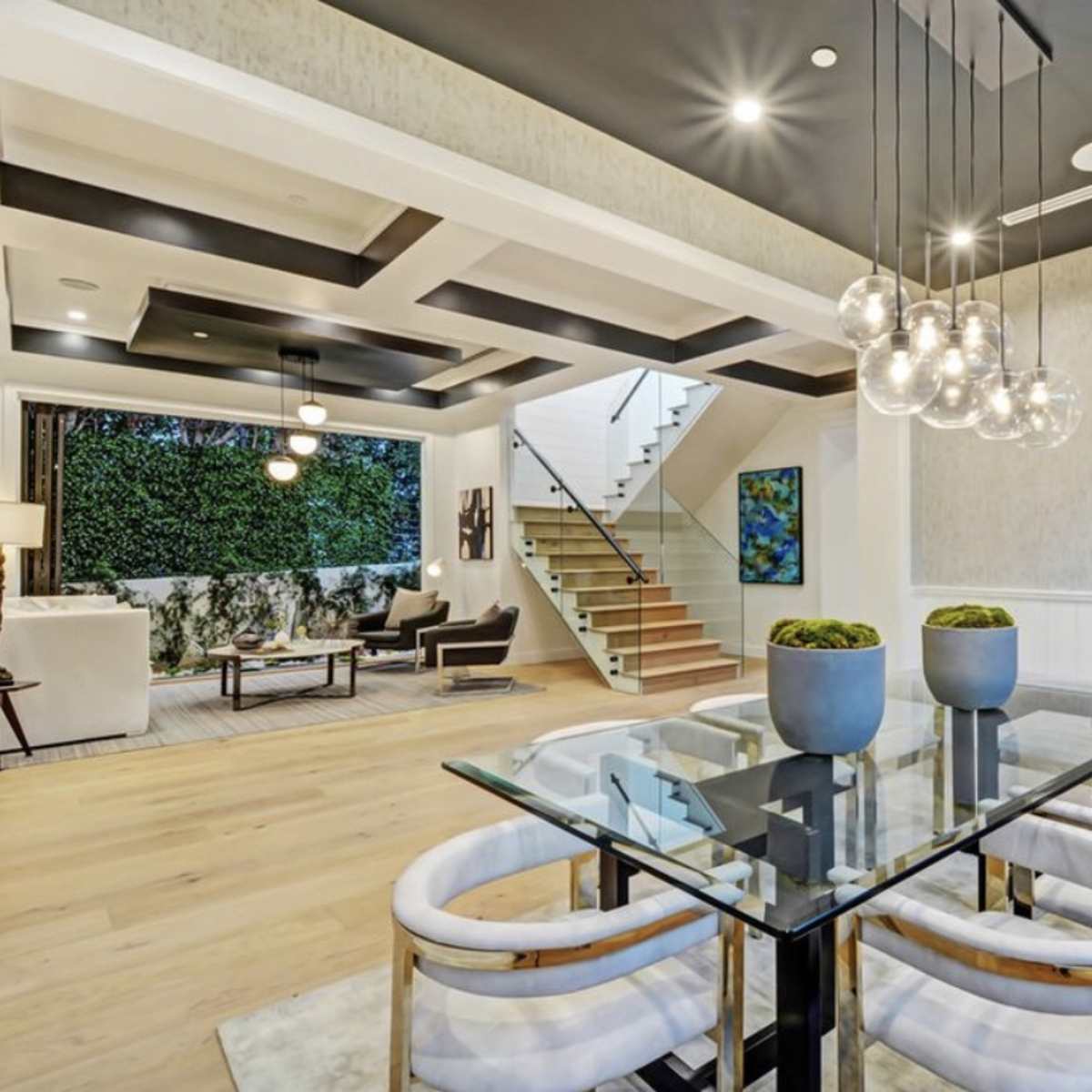 A modern open-concept living and dining area with a sleek glass dining table, stylish chairs, and a staircase leading to an upper level.
