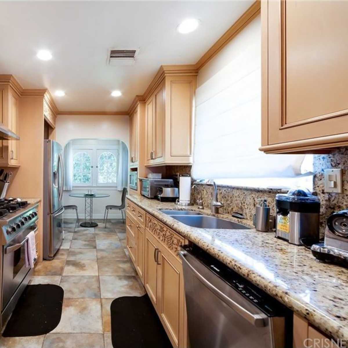 The kitchen features light wood cabinetry, granite countertops, and stainless steel appliances, with a window overlooking an outdoor area.