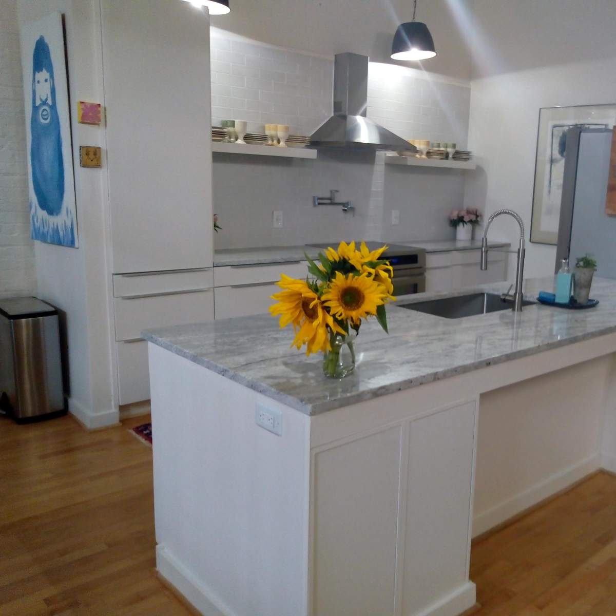 A modern kitchen with a marble countertop, stainless steel appliances, and a vase of sunflowers on the island.