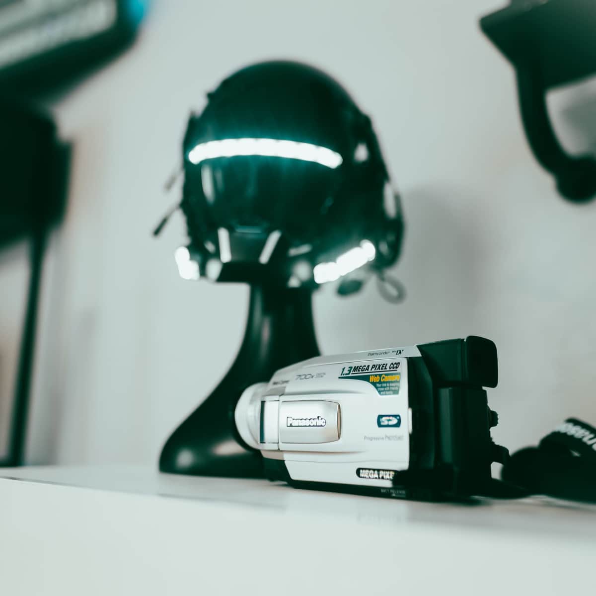 A Panasonic camcorder sits on a shelf next to a reflective helmet on a black stand.