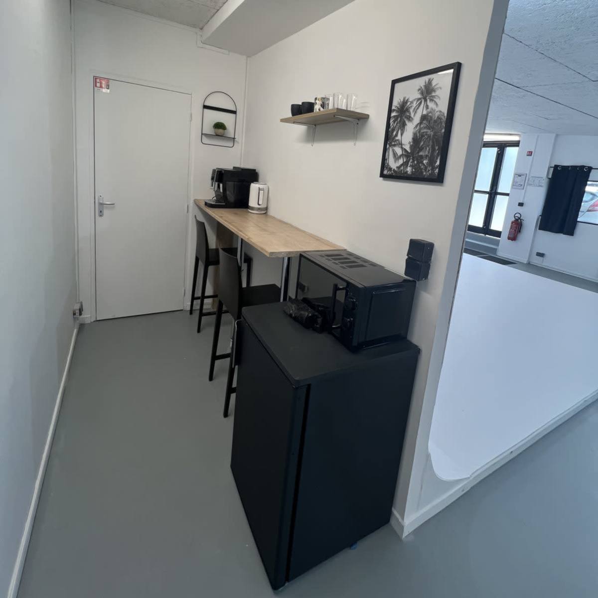 A kitchenette area features a wooden countertop with bar stools, coffee machines, and a microwave, alongside a door leading to another room.