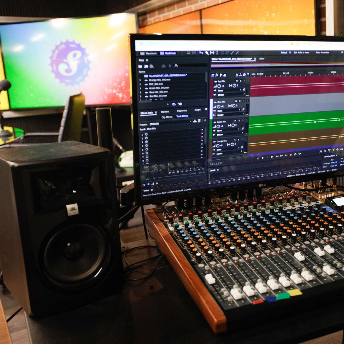 A sound mixing console with a computer screen displaying audio editing software, set in a recording studio environment.