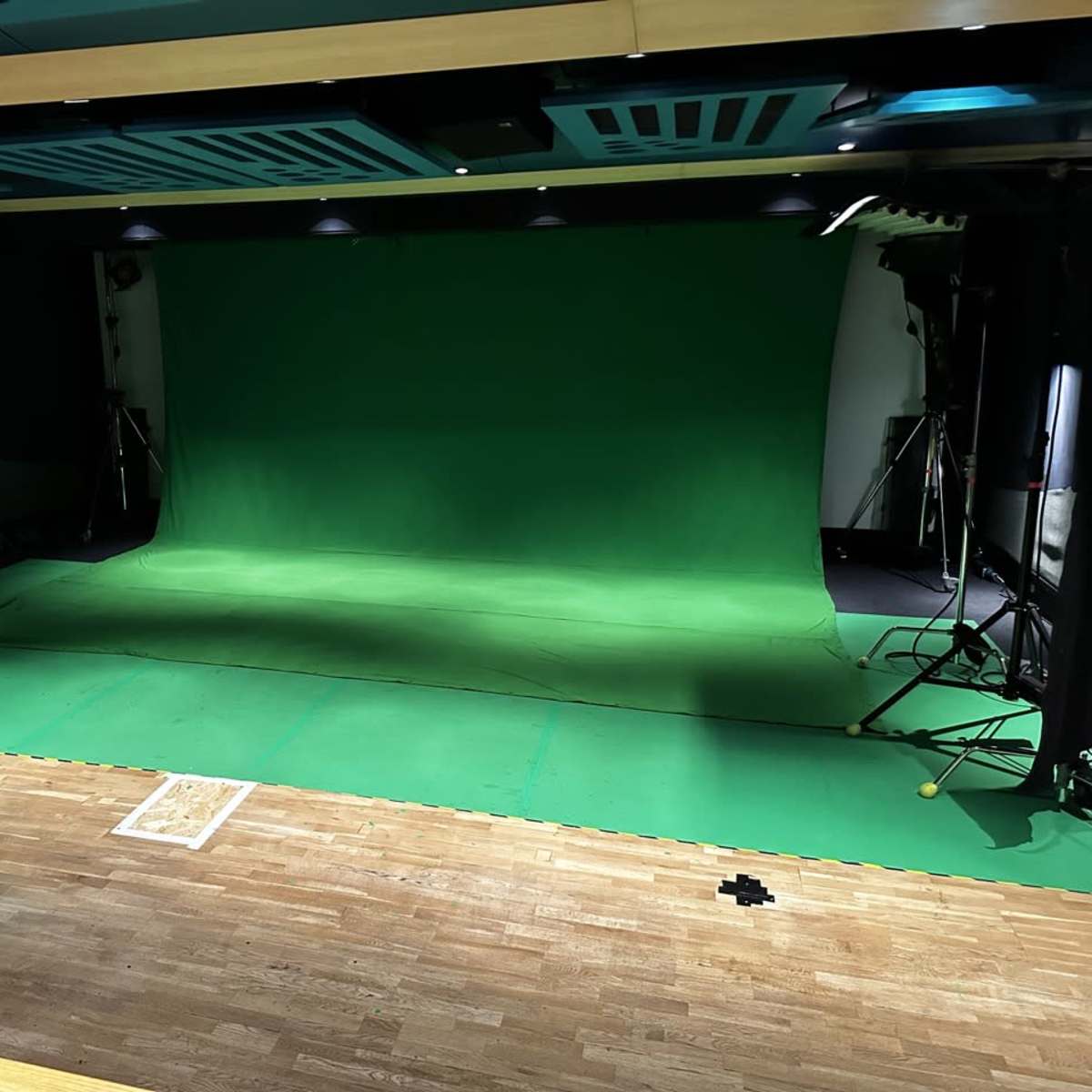 A green screen studio setup with lighting equipment arranged around a large green backdrop on a wooden floor.