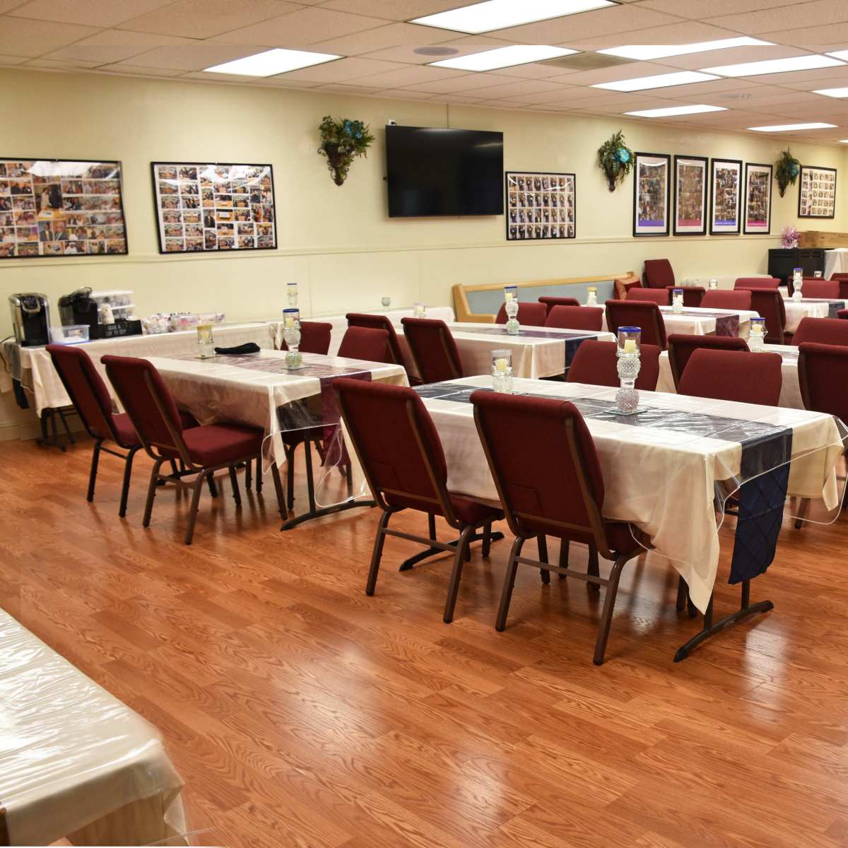 A spacious dining area with several tables covered in white tablecloths and arranged with chairs facing each table, surrounded by walls adorned with framed photographs.