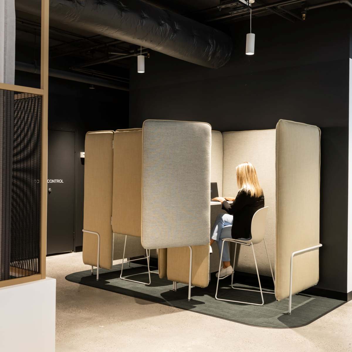 A person sits in a private cubicle with tall fabric partitions in a modern office space.