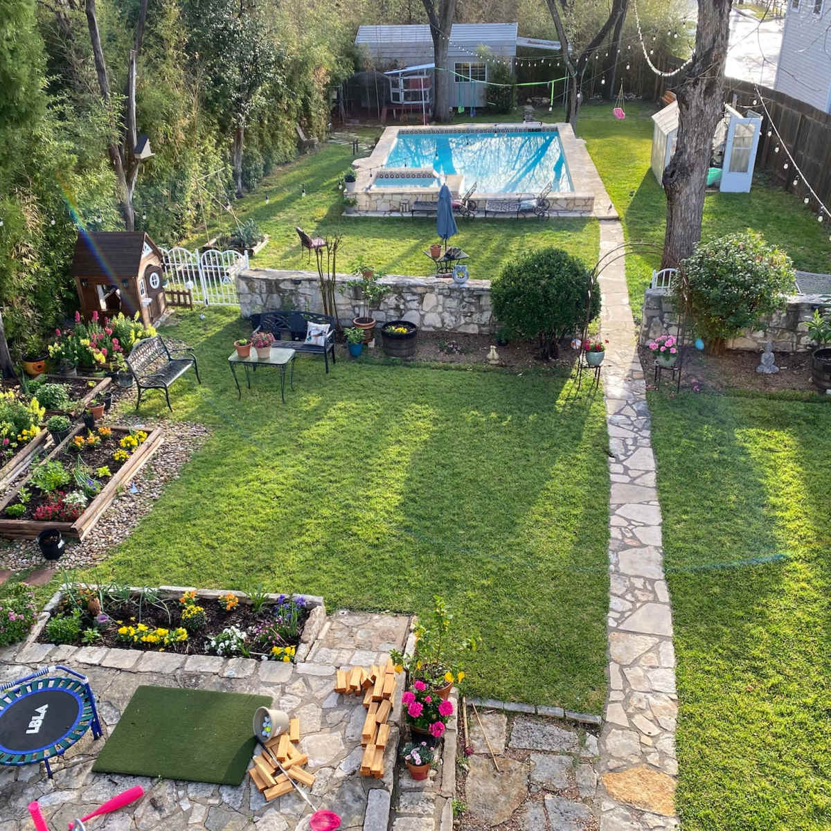 A well-maintained backyard with a swimming pool, a stone pathway, and neatly arranged flower beds.