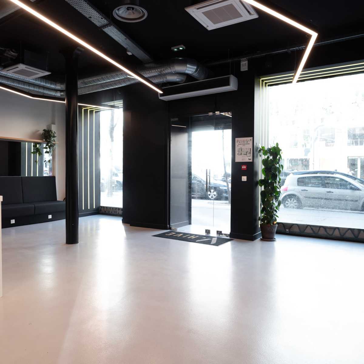 A spacious, modern lobby with large windows, a reception area, and plants positioned around the room.