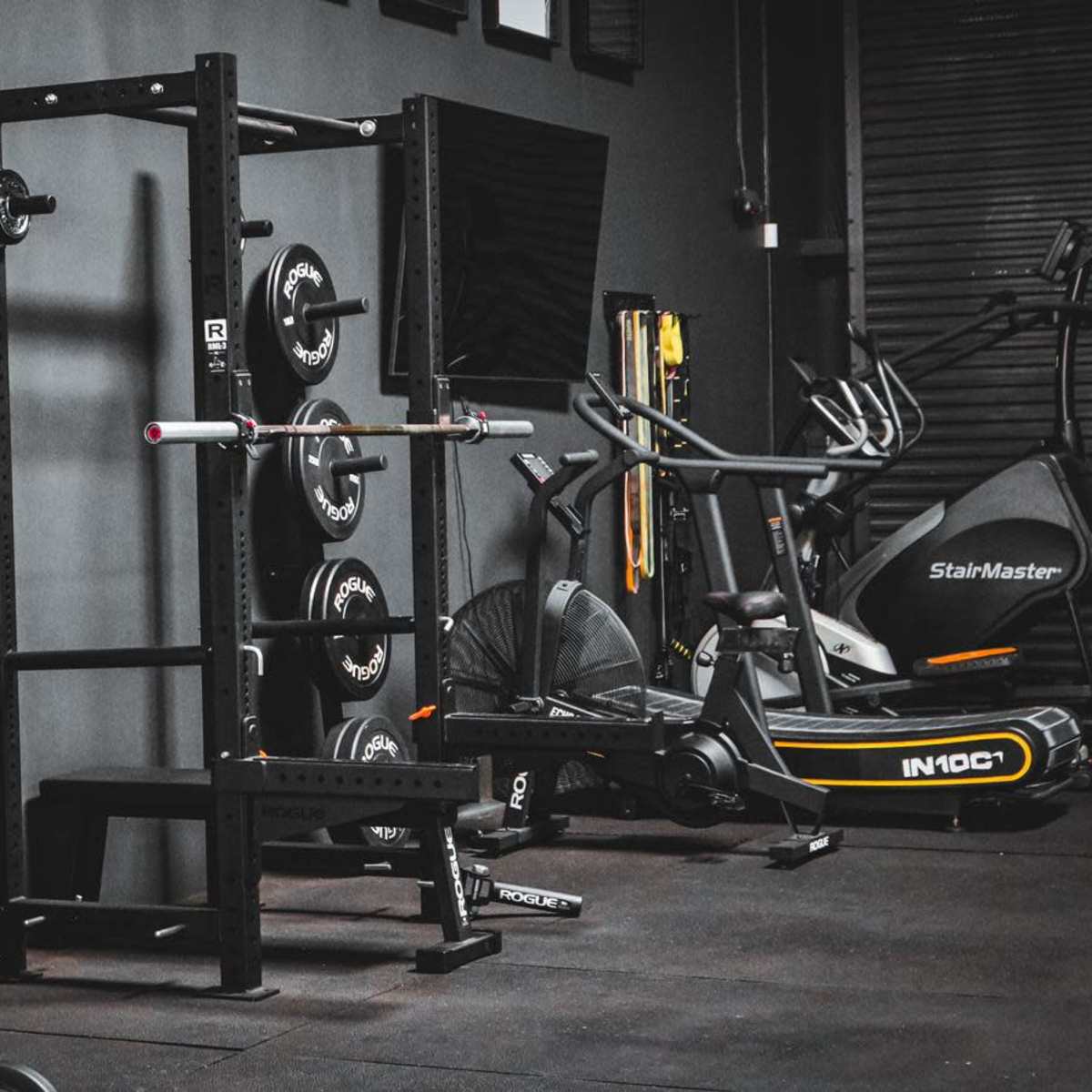 A gym interior featuring various exercise equipment including a squat rack, weight plates, and an elliptical machine.