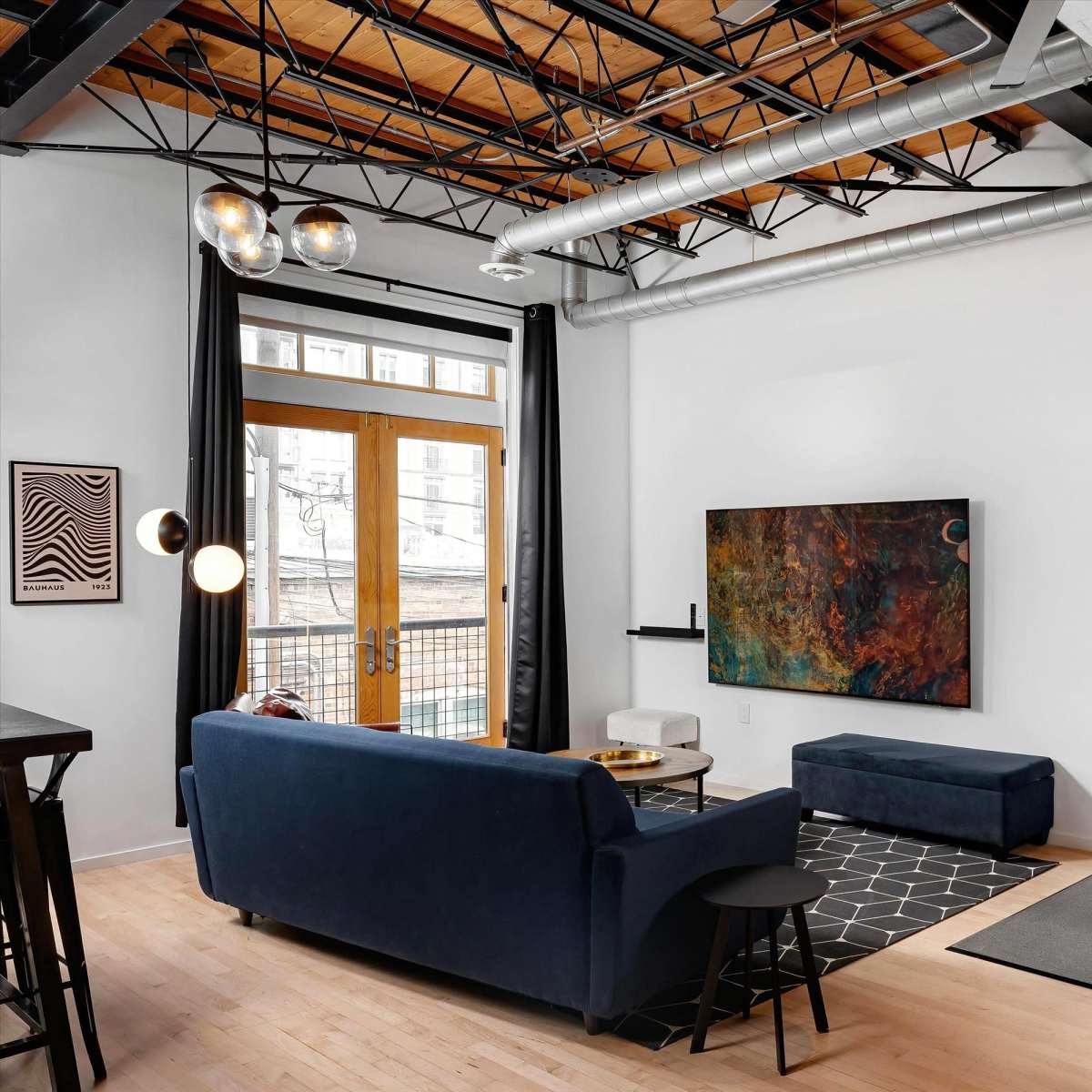 A modern living room featuring a blue couch, a wall-mounted television, a coffee table, and a colorful abstract artwork.