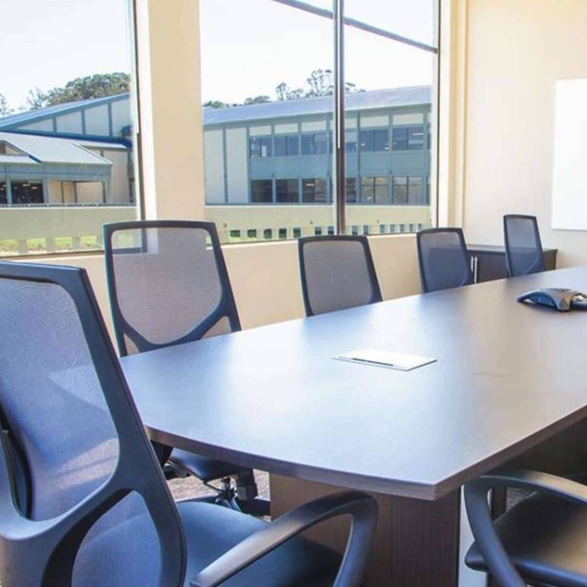 A modern conference room features a large table surrounded by several ergonomic chairs, with windows displaying a view of the outdoors.