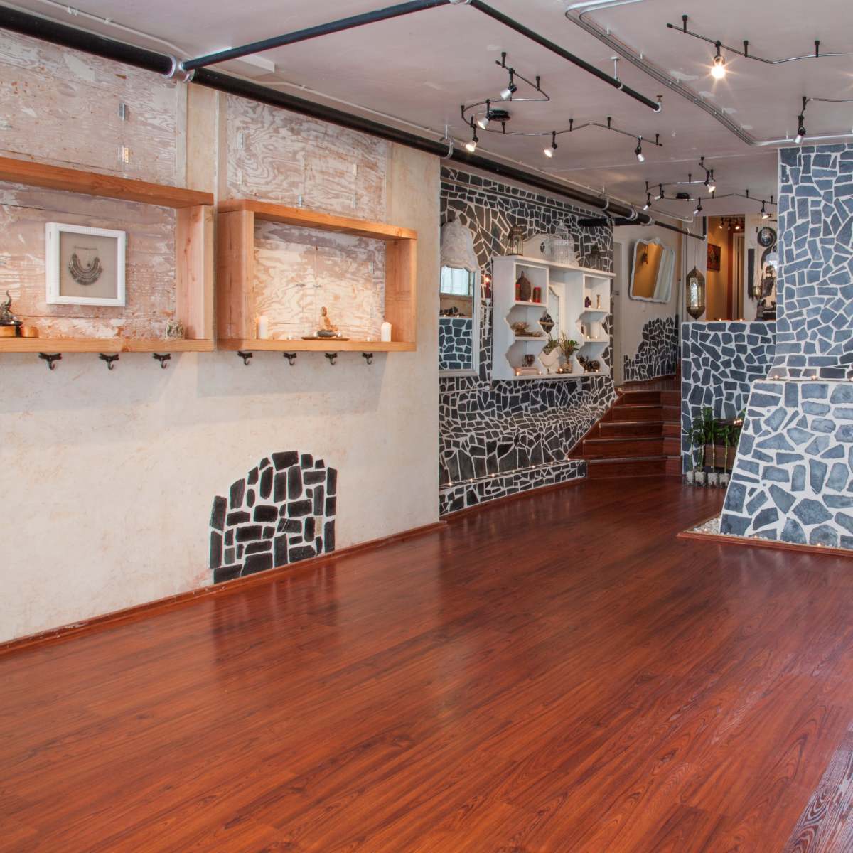 A spacious room with wooden flooring, featuring walls decorated with irregular stone patterns and wooden shelves displaying various artworks.