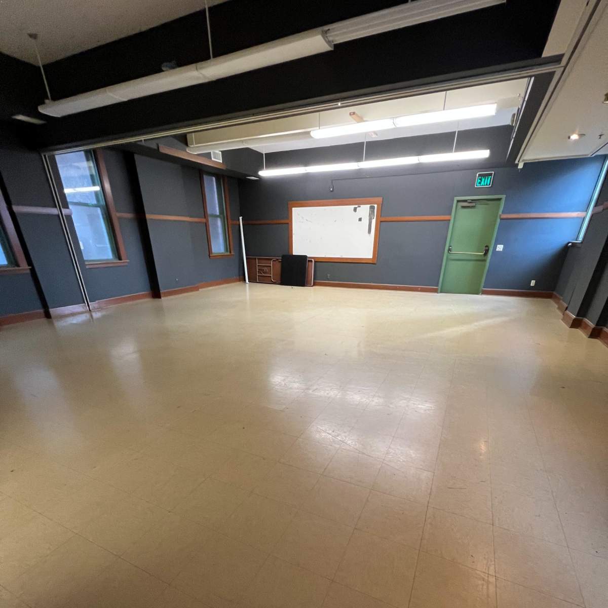 An empty classroom with a bare floor, a whiteboard on the wall, and a closed door.