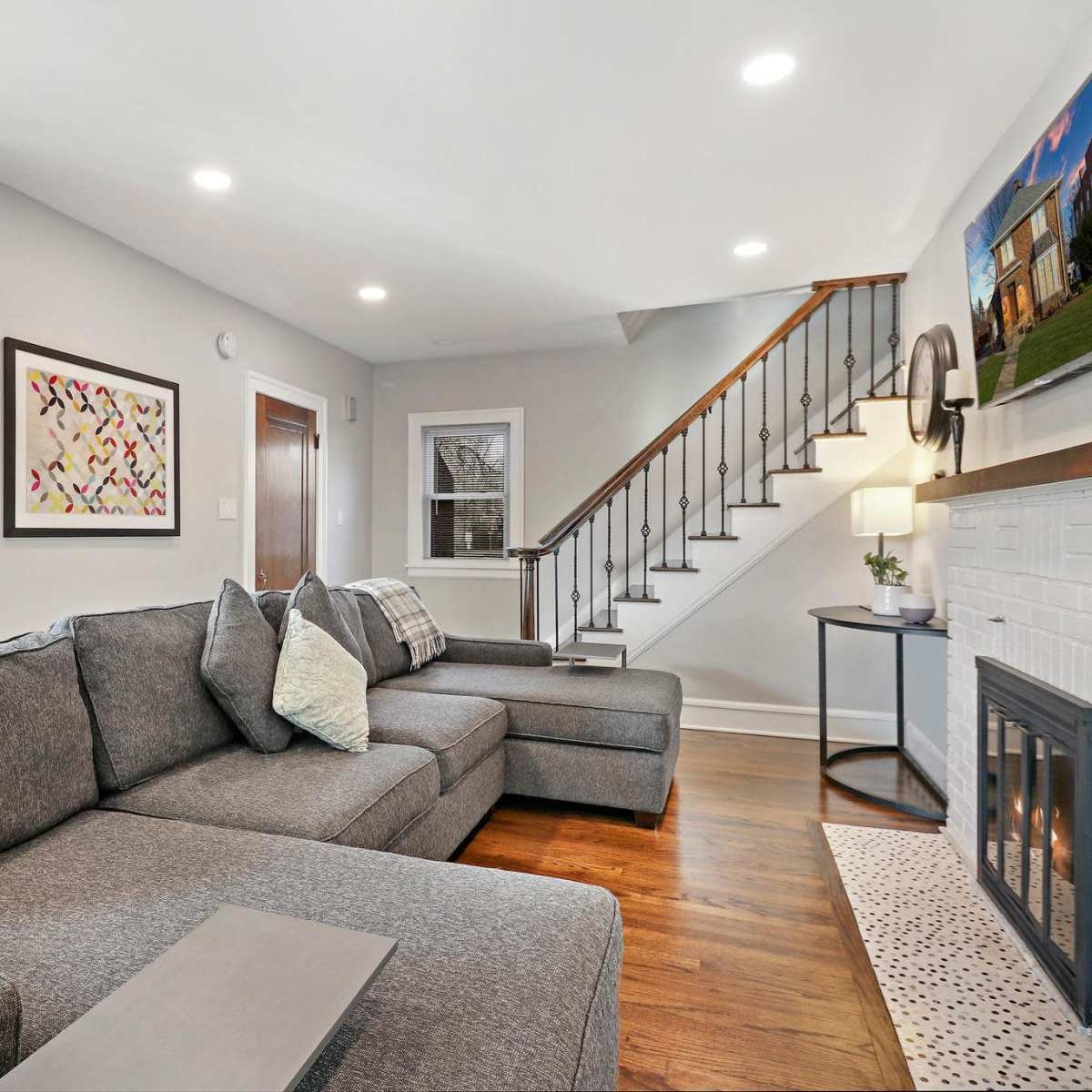 The living room features a gray sectional sofa, a fireplace with a decorative front, and a staircase leading to the upper level.