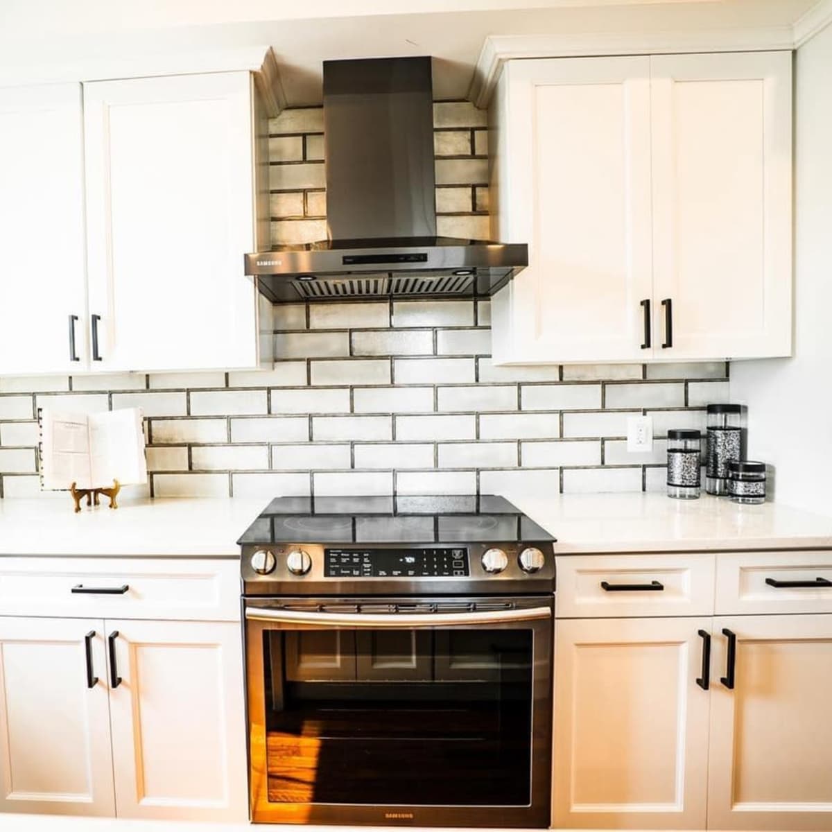 The kitchen features white cabinets, a stainless steel oven, a tile backsplash, and a range hood.