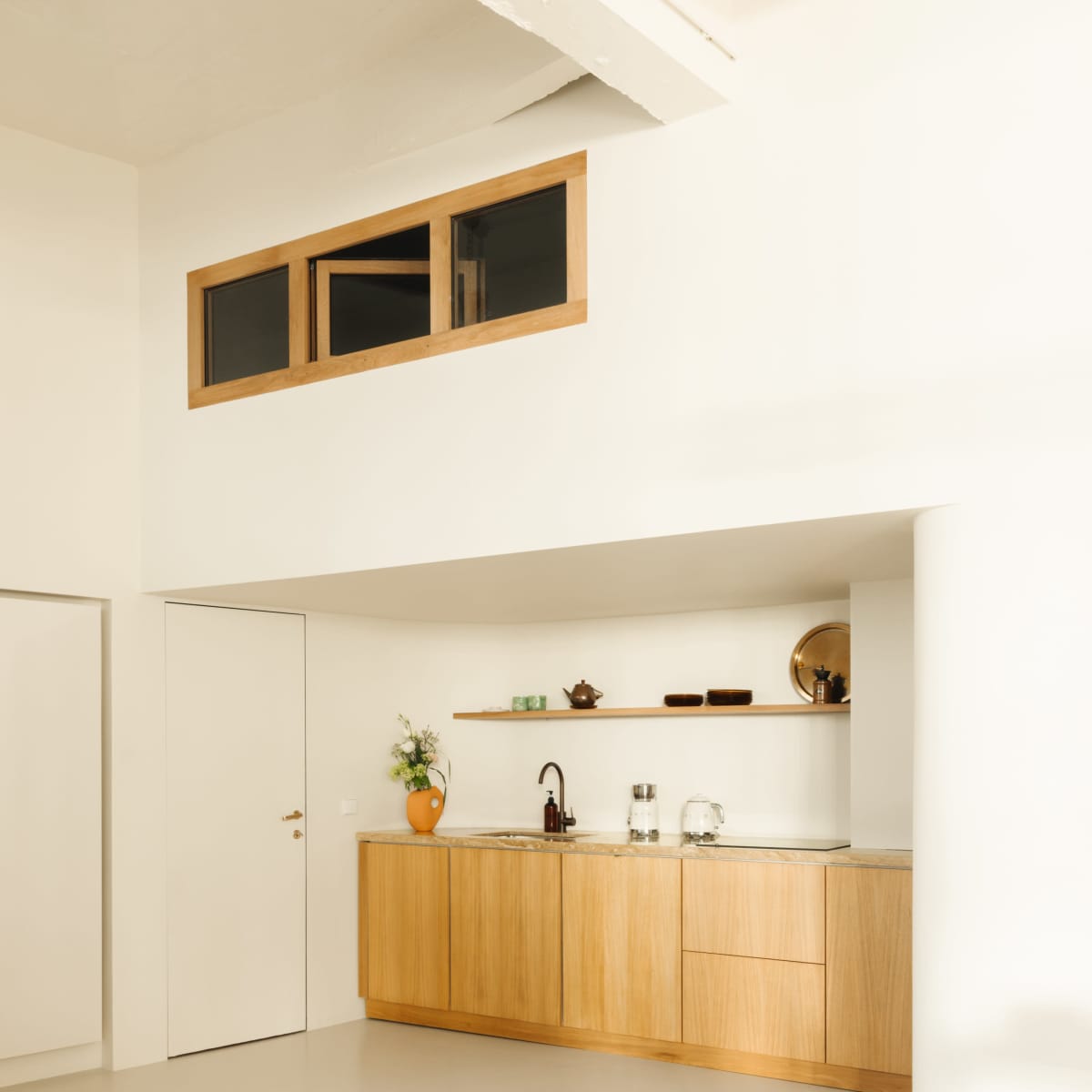 A modern kitchen with wooden cabinetry, a sink, and minimal decorative items against a white wall.