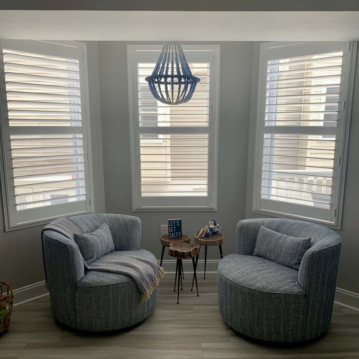 Two upholstered chairs are positioned beside a small table in a well-lit corner, featuring a patterned throw and a modern chandelier above.