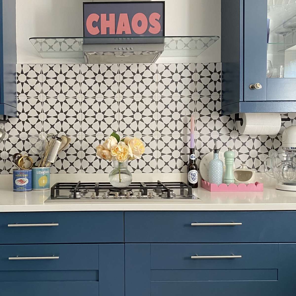 A modern kitchen features blue cabinetry, a patterned tile backsplash, a gas stovetop, and various kitchen appliances on the counter.