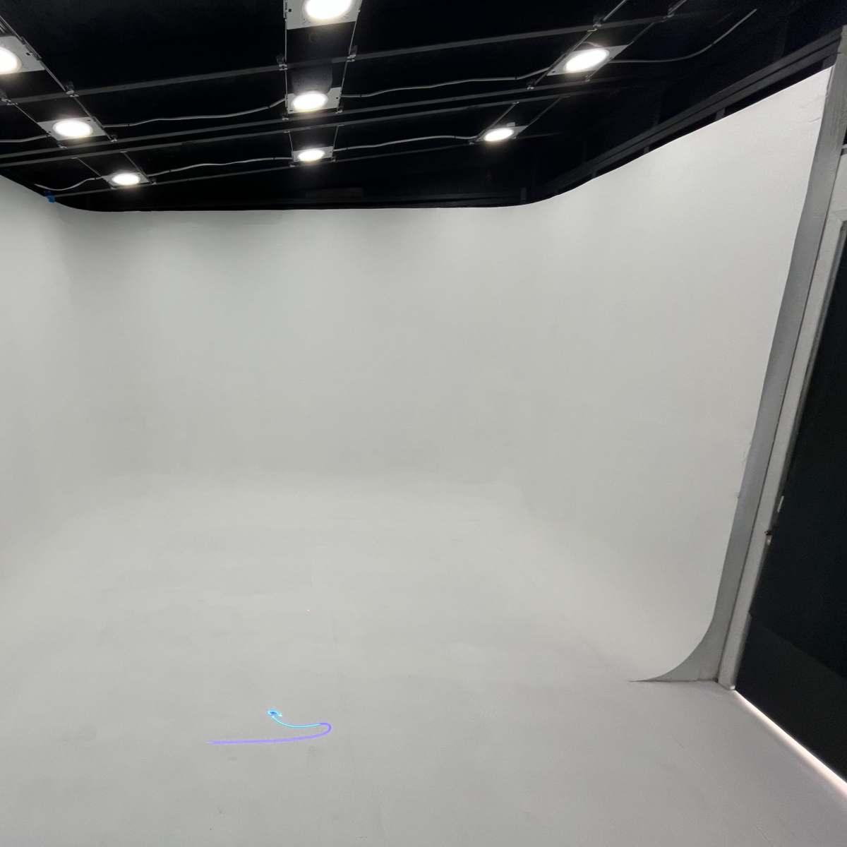 A clean, empty studio space with white walls and a seamless backdrop, illuminated by overhead lights.