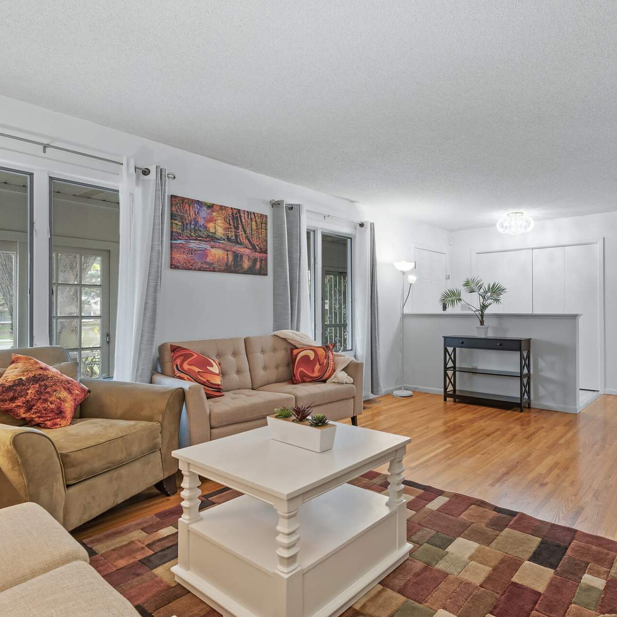 A bright living room with two sofas, a coffee table, and a bar area, featuring wooden floors and large windows.