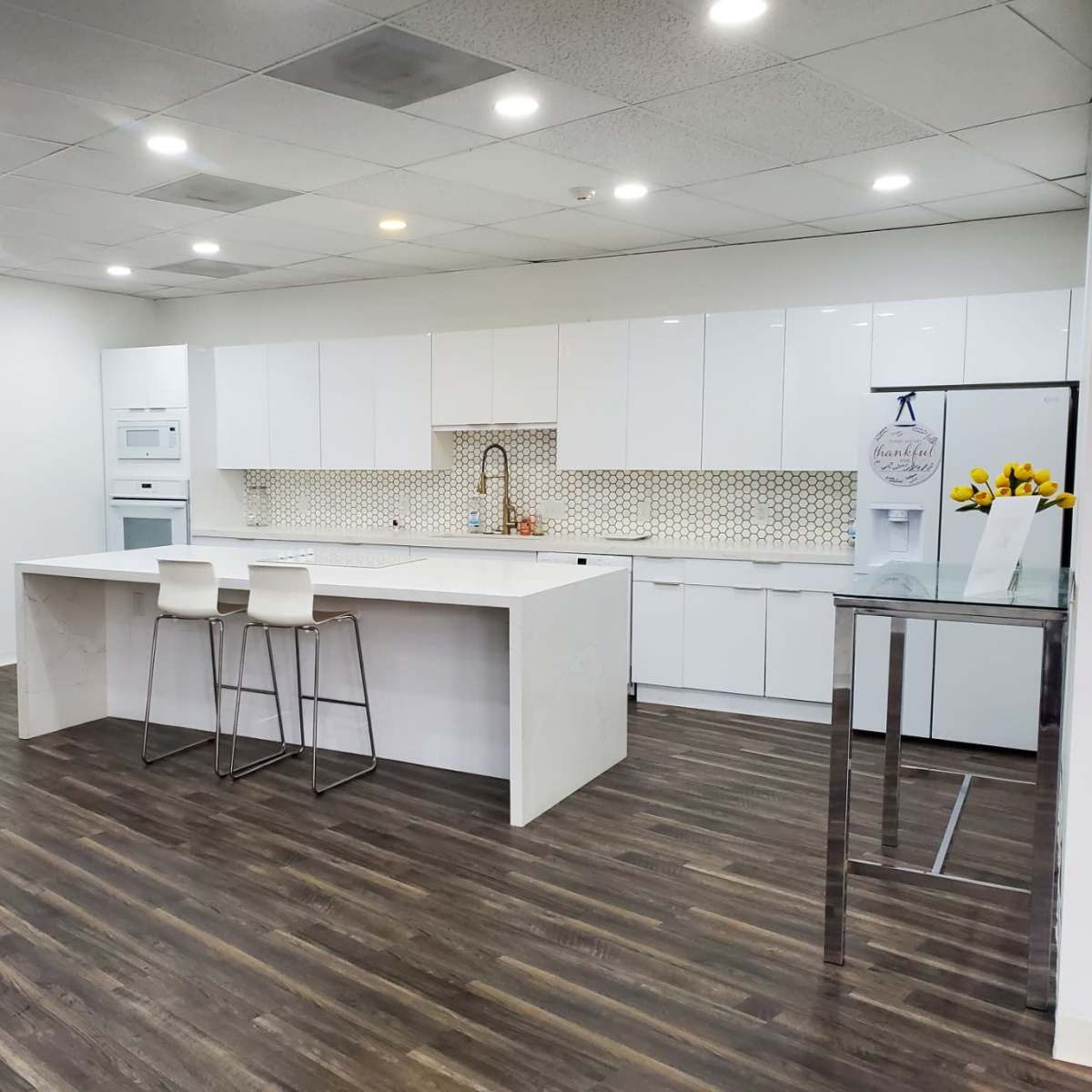 A modern kitchen with white cabinetry, a large island with two stools, and a wall-mounted television.