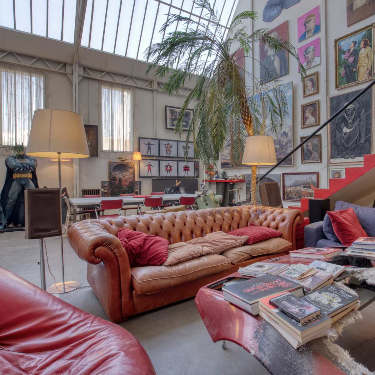 A spacious indoor living area with a mix of modern furniture, several artworks on the walls, and a staircase leading to an upper level.