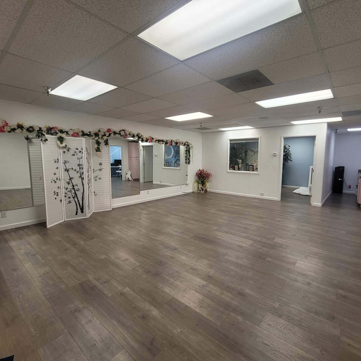 An empty spacious room with wooden flooring, wall mirrors, decorative partitions, and light-colored walls.