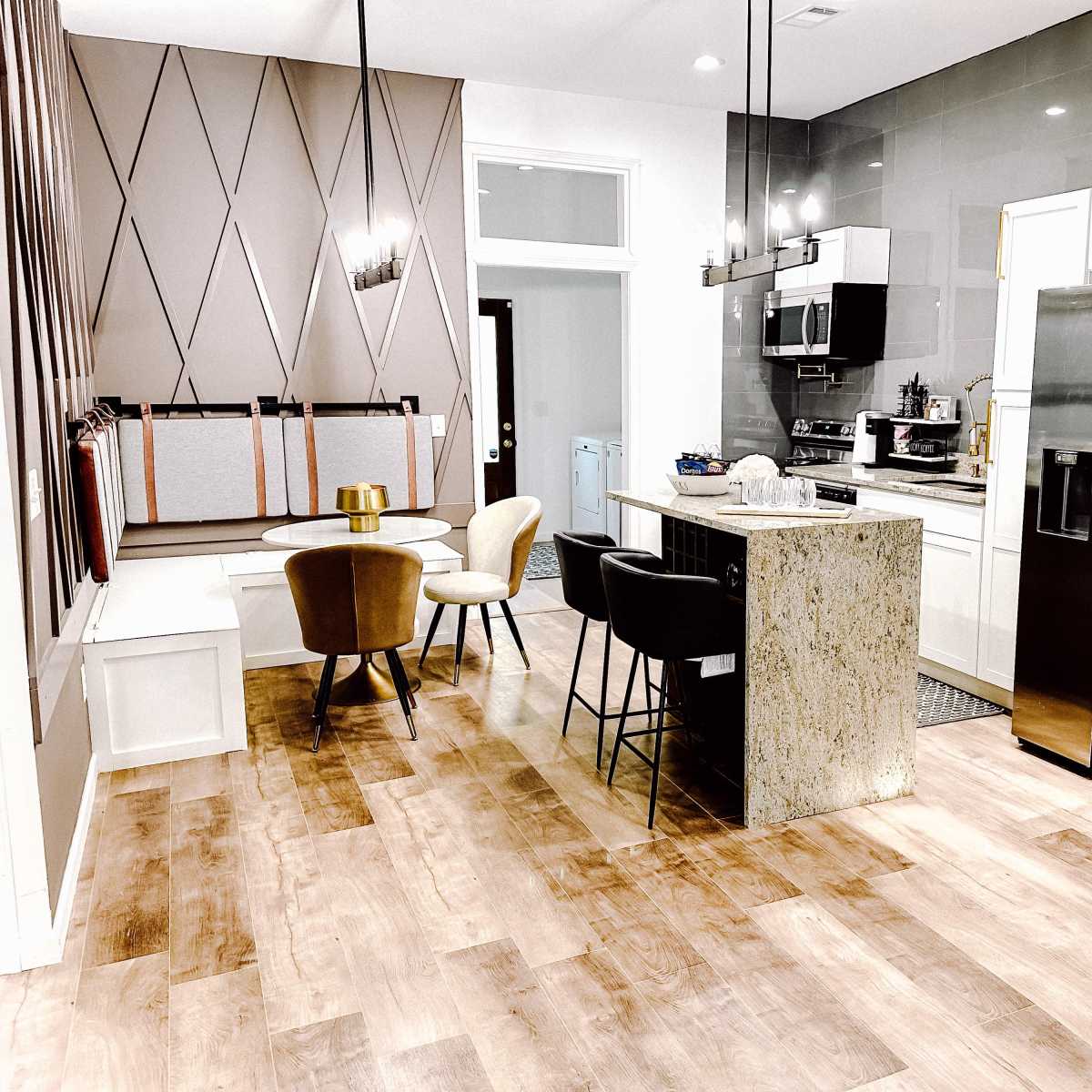 A modern kitchen and dining area featuring a stone island, four chairs around a small dining table, and stainless steel appliances.