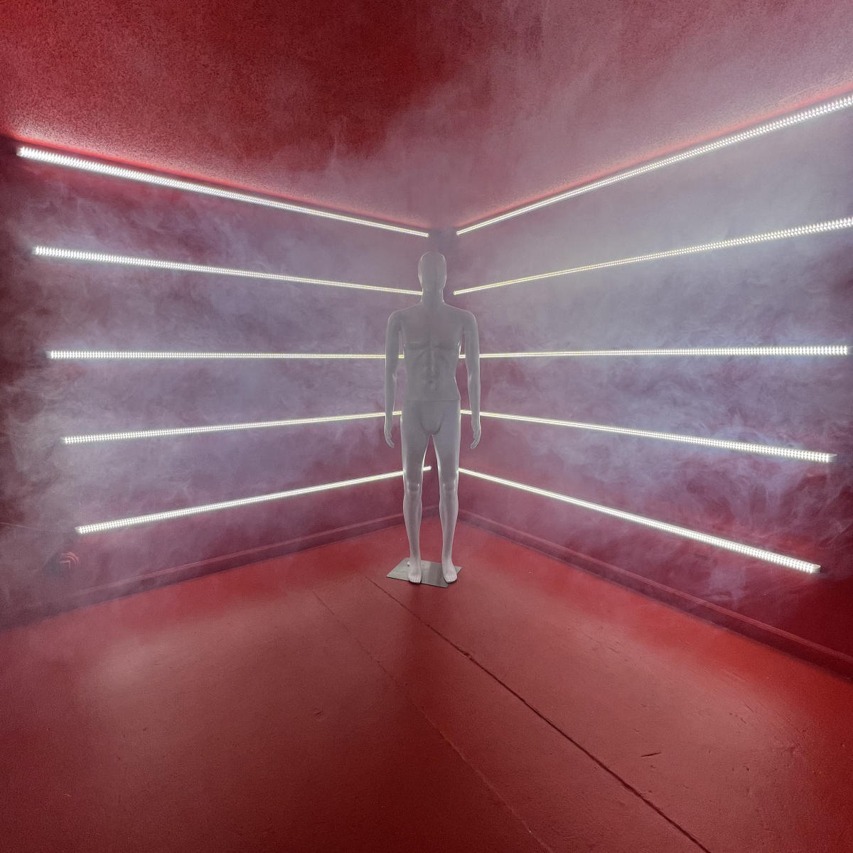 A white mannequin stands in a fog-filled room illuminated by colored LED strips along the walls.