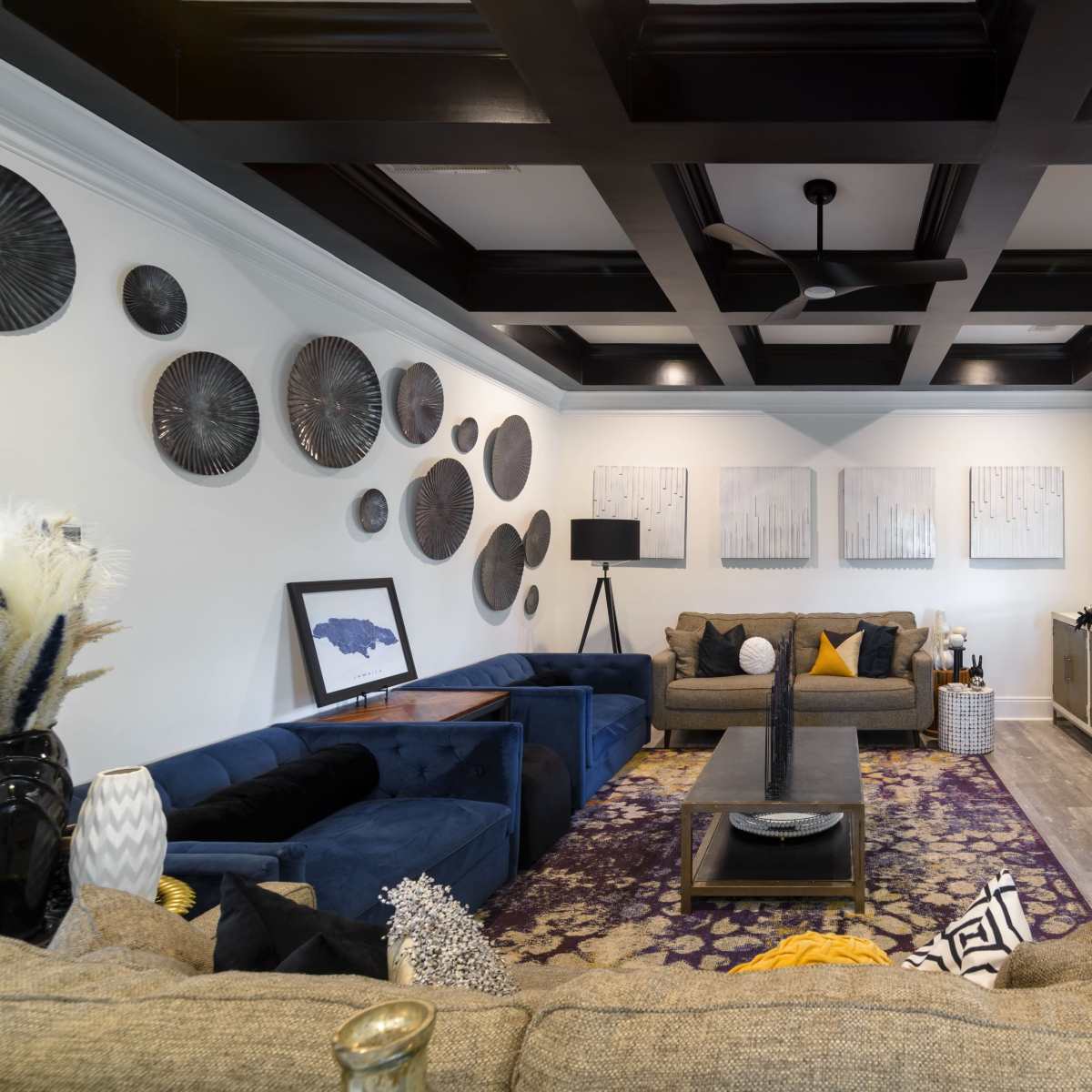 The living room features a mix of dark and light furnishings, with a large sectional sofa, a coffee table, and wall art arranged around a fireplace and a television mounted above it.
