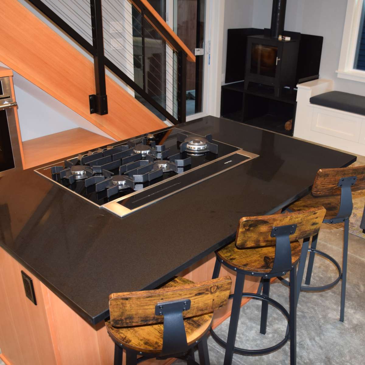 A modern kitchen with a central island featuring a stovetop, surrounded by three bar stools, and a cozy seating area in the corner.