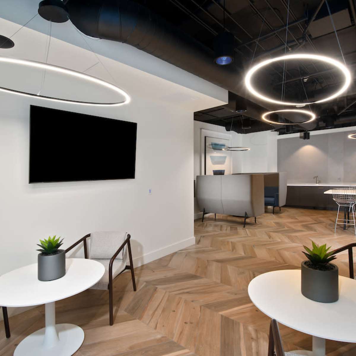 A modern interior space with two circular light fixtures, light wood flooring, and a seating area that includes two small tables and chairs.