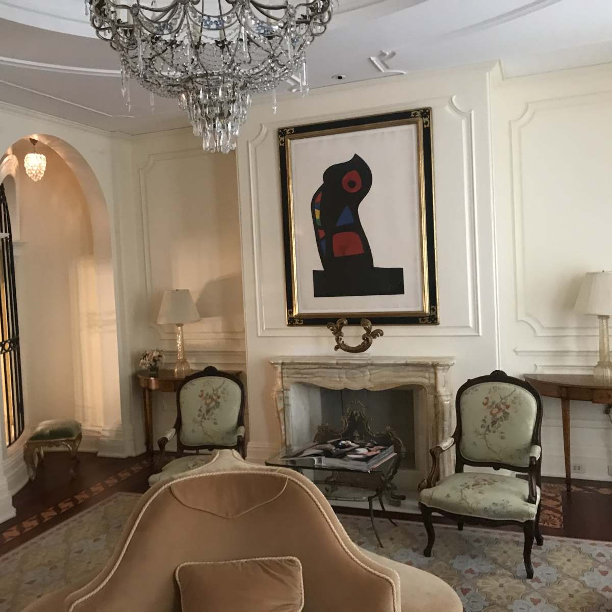 An elegantly designed room featuring a chandelier, a framed artwork, and two floral-patterned armchairs arranged near a fireplace.