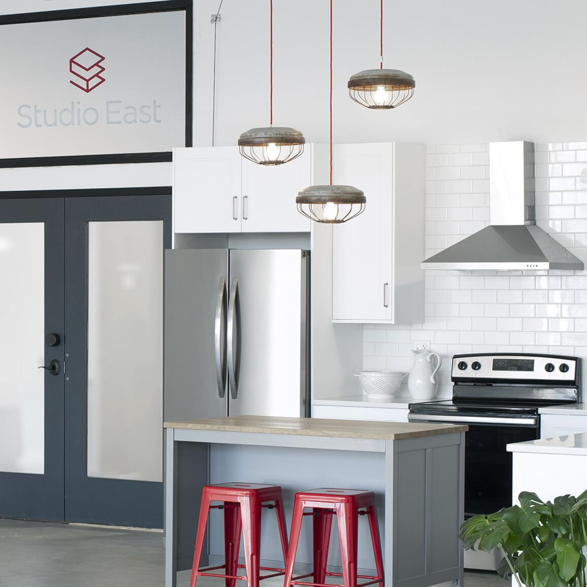A modern kitchen with a wooden island, two red metal stools, stainless steel appliances, and pendant lighting.