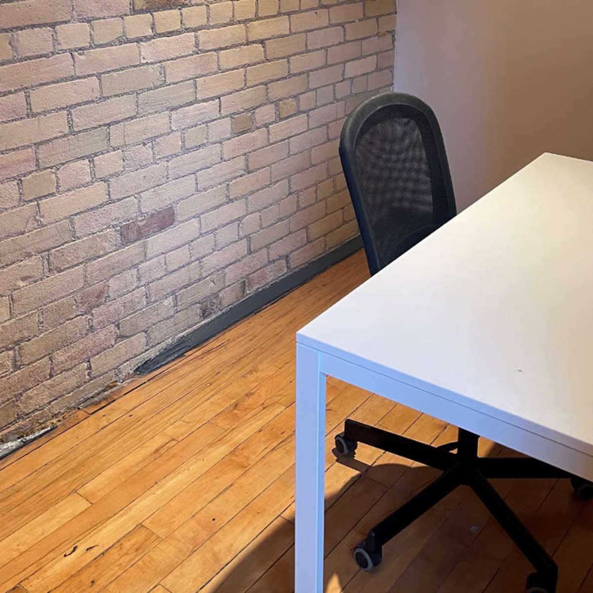 A simple desk and a chair in a room with a brick wall and hardwood floor.