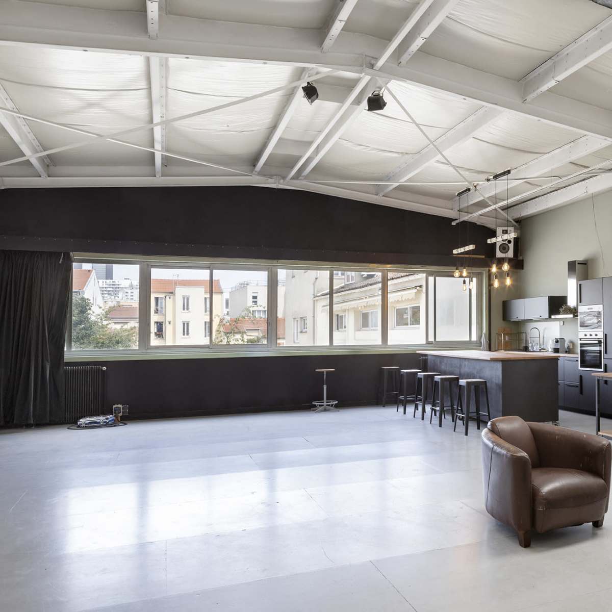 A spacious, modern open-concept living area with a kitchen, seating area, and large windows overlooking a cityscape.