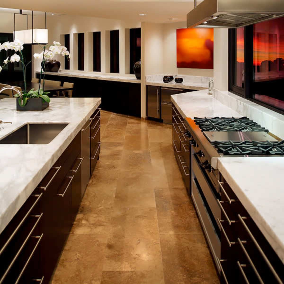 A modern kitchen features sleek cabinets, a marble countertop, and a central island with a gas stove, illuminated by overhead lights.