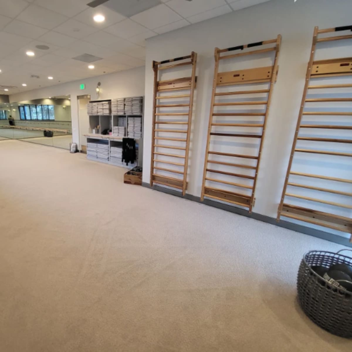 A spacious exercise studio with wooden wall bars, a large mirror, and neatly organized storage cubicles.