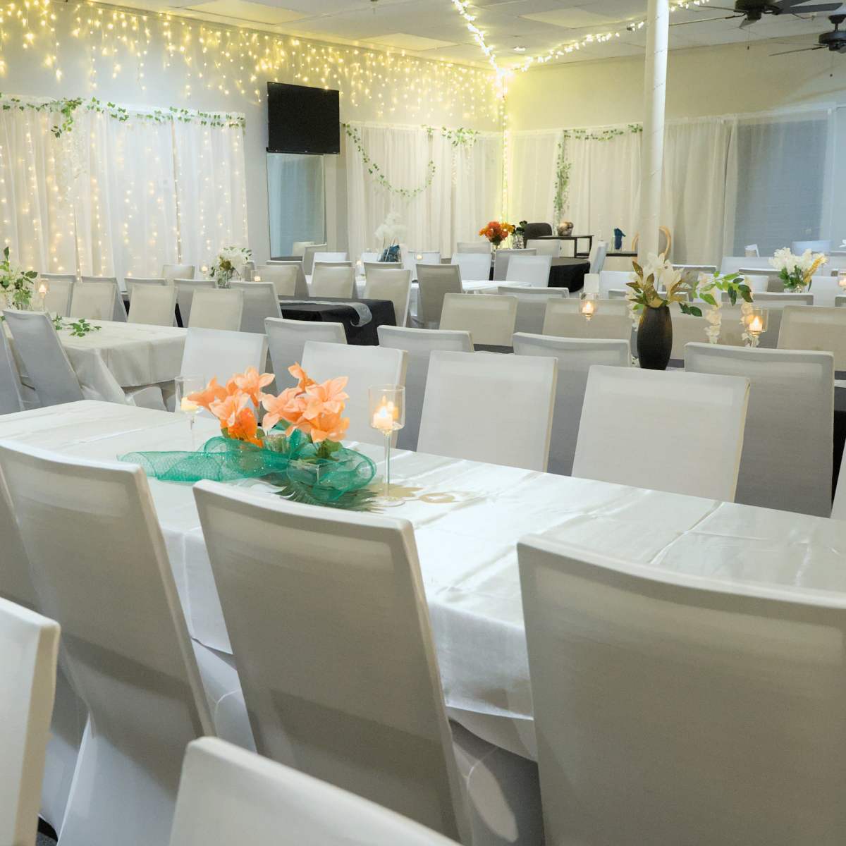 A banquet hall set with white tables and chairs, decorated with flowers and soft lighting.