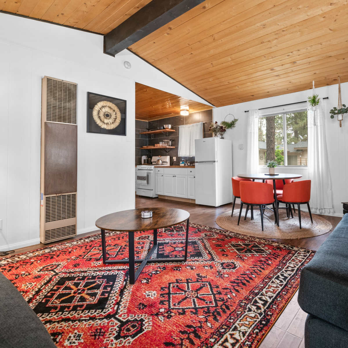 A modern living room with a wooden ceiling, a cozy seating area, a dining table for four, and a fireplace.