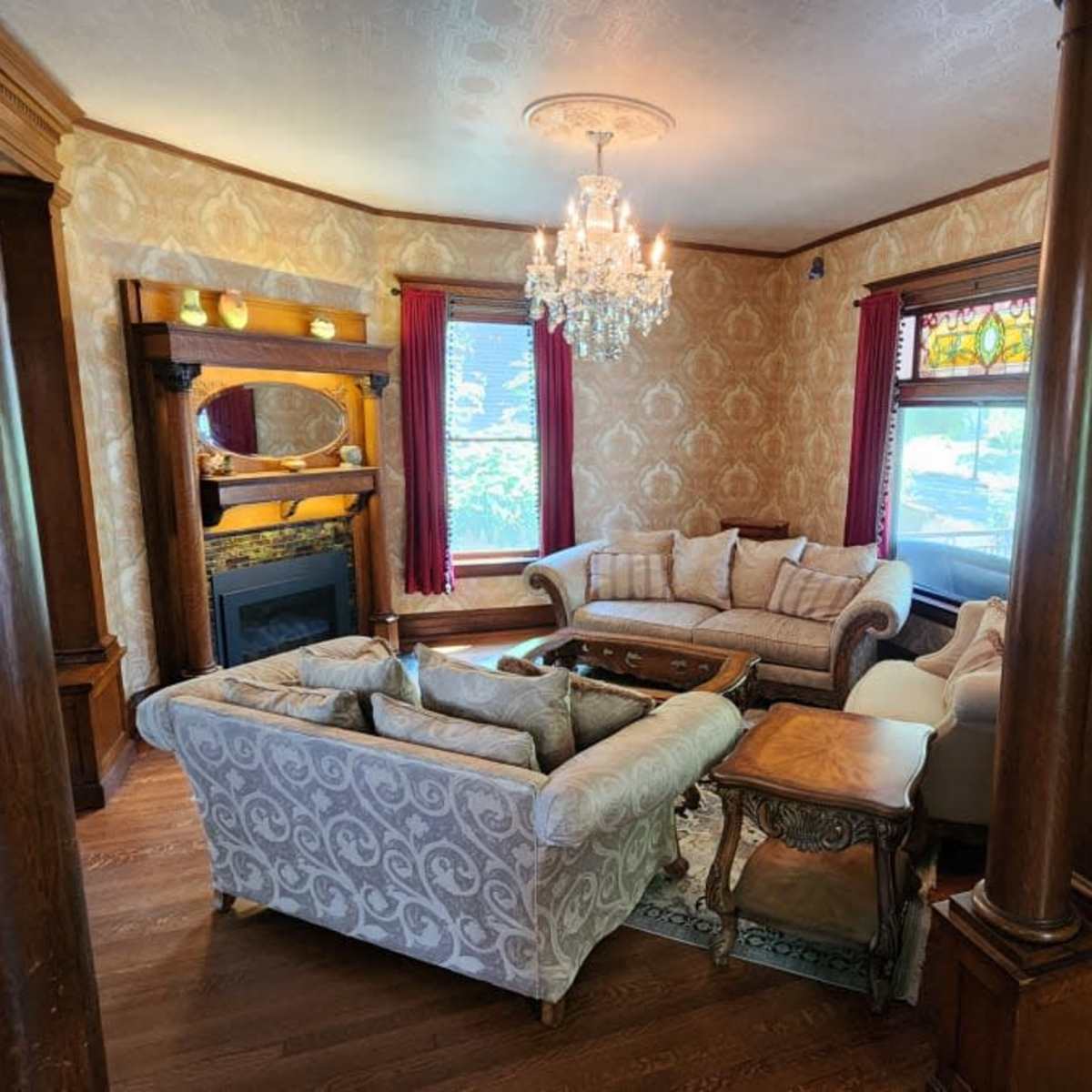A living room with light-colored walls, two sofas, a coffee table, and a chandelier, surrounded by wooden columns and stained glass windows.