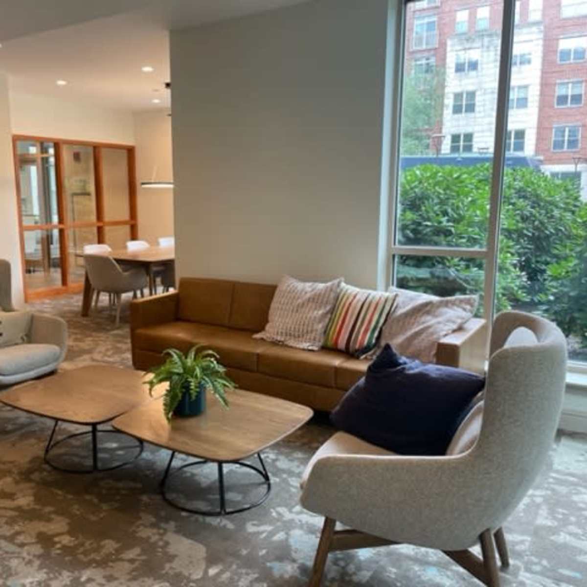 A cozy lounge area with a brown sofa, two armchairs, and a coffee table surrounded by large windows.