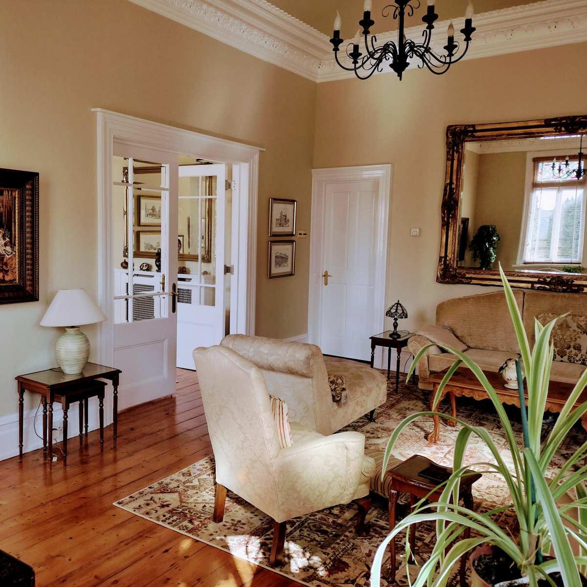 A well-furnished living room with a chandelier, a large mirror, and seating arranged around a central area.