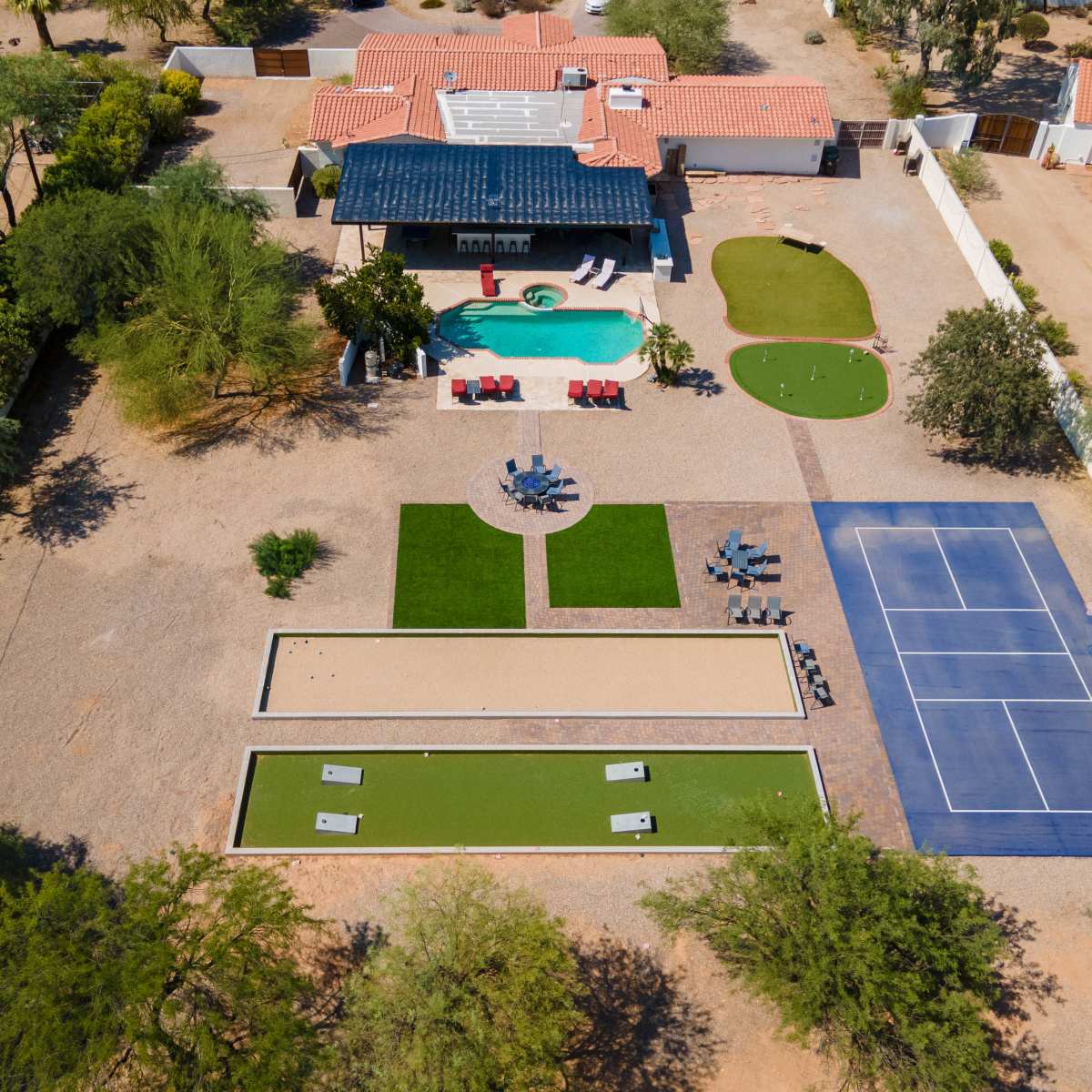An aerial view of a spacious property featuring a swimming pool, a lawn area, a tennis court, and various seating arrangements.