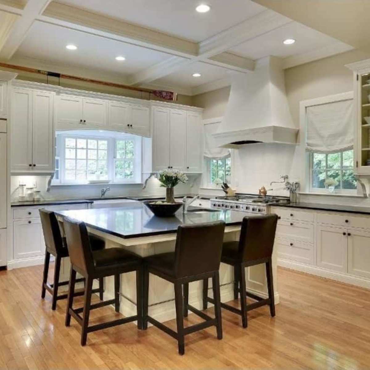 A modern kitchen features white cabinetry, a central island with seating, and hardwood flooring.