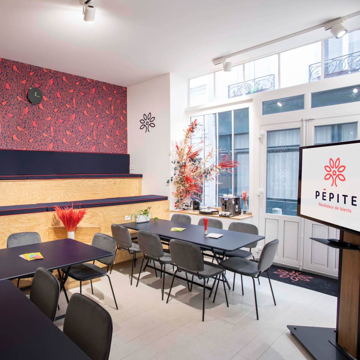 A modern meeting room with wooden and dark furniture, decorated with a patterned wallpaper and vibrant floral arrangements.