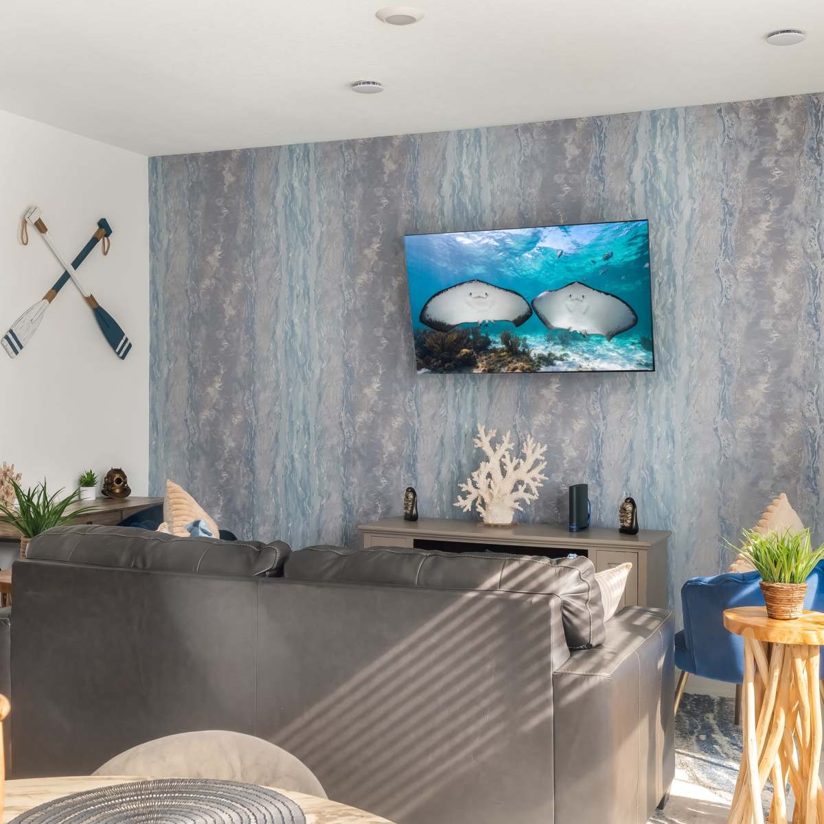 A modern living room with a dark leather sofa, a wall-mounted television displaying an underwater scene, and decorative elements like plants and marine-themed decor.