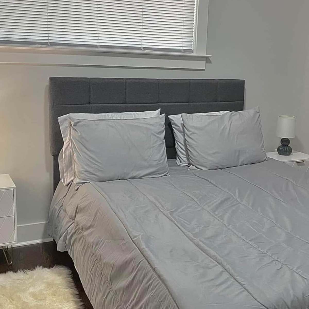 A neatly made bed with gray bedding and two pillows is positioned against a wall in a well-lit bedroom.