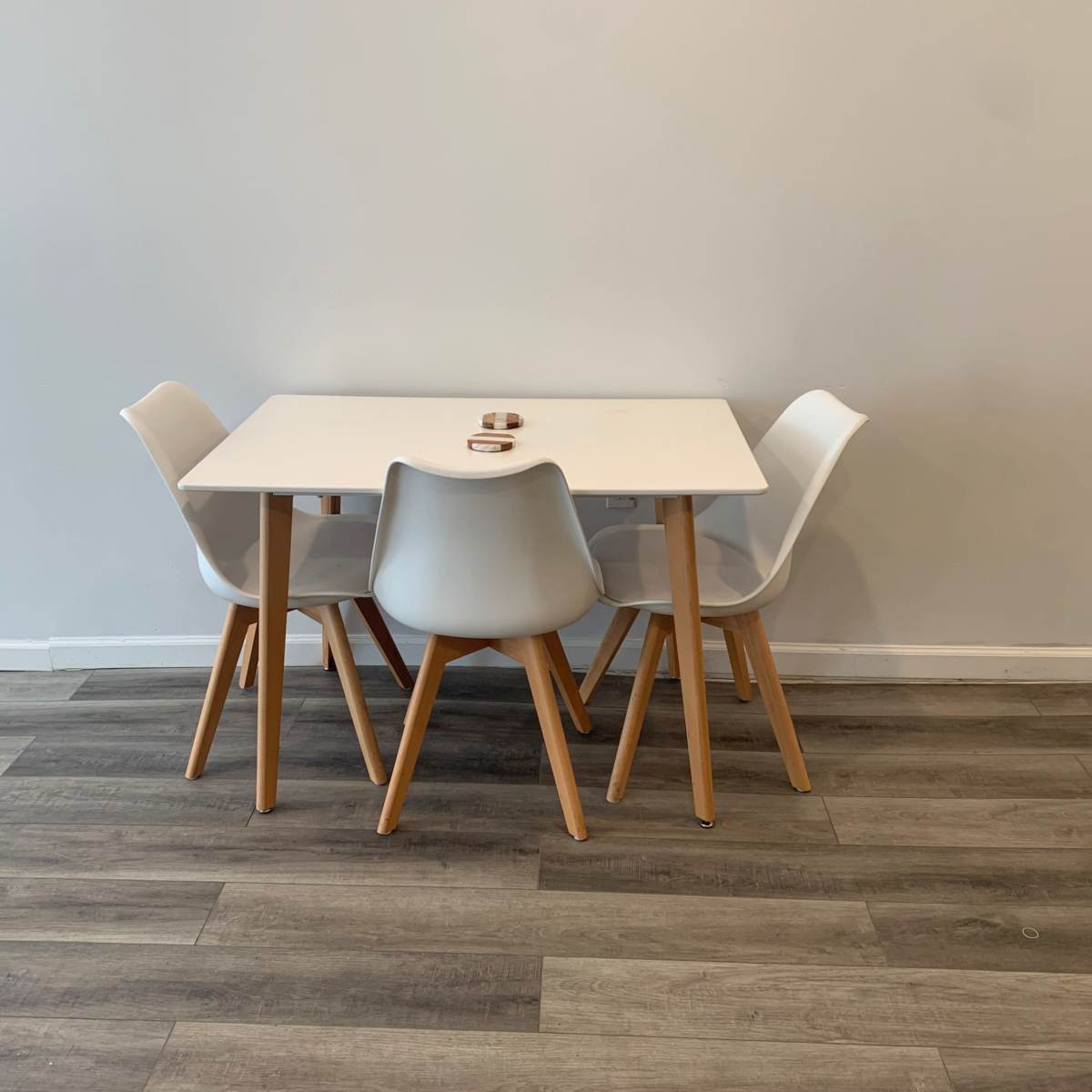 A rectangular white table is set with three matching white chairs on a wood-look floor against a plain wall.