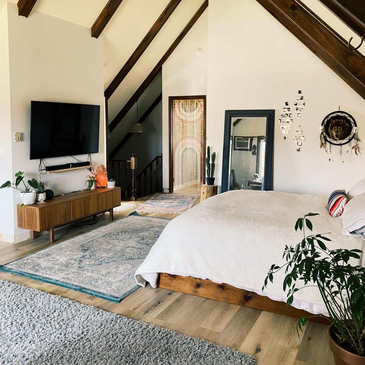 A spacious bedroom features a wooden bed, a large TV mounted on the wall, and a staircase leading to an upper level.