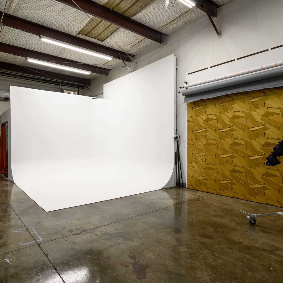 A photography studio with a large white backdrop and a textured brown wall on one side.